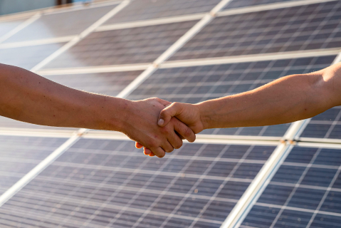 Handschlag vor Solarpaneelen - Alles aus einer Hand - Nachhaltige Energie aus der Nachbarschaft
